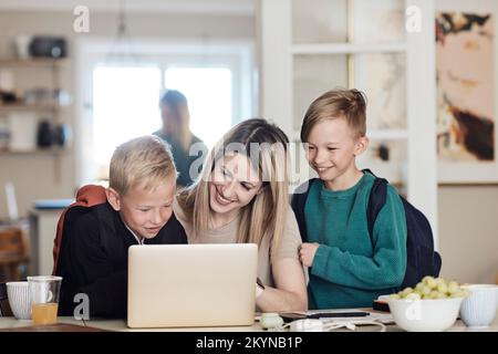 Glückliche Mutter mit aufgeregten Söhnen, die sich zu Hause ein Notebook ansehen Stockfoto