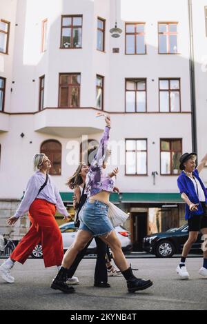 Junge LGBTQIA-Freunde, die während der Schwulenparade auf dem Fußweg spazieren gehen Stockfoto