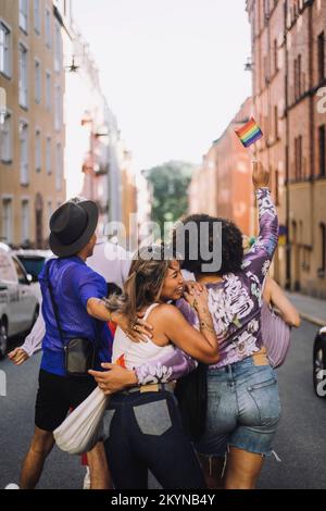 Glückliche junge Freunde, die während der Schwulenparade auf der Straße spazieren gehen Stockfoto