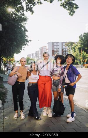 Ein langes Porträt von lächelnden jungen LGBTQIA-Freunden, die auf dem Fußweg stehen Stockfoto