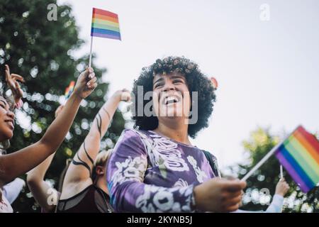 Glückliche Transgender-Frau mit Regenbogenflagge, die sich an der Schwulenparade erfreut Stockfoto