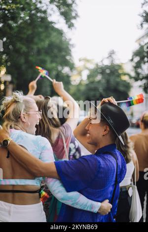 Glücklicher junger Mann mit Hut, während er mit einer Freundin die Schwulenparade genießt Stockfoto