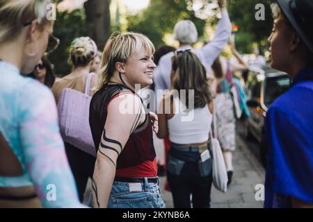 Glückliche, nicht binäre Person, die mit männlichen und weiblichen Freunden unterwegs ist Stockfoto