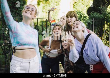 Glückliche Frau, die Selfie mit Freunden macht, Gesten macht und ein Friedenszeichen zeigt Stockfoto