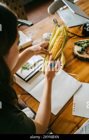 Aus dem Blickwinkel eines weiblichen Stylissins, der frischen Mais am Tisch im Studio untersucht Stockfoto