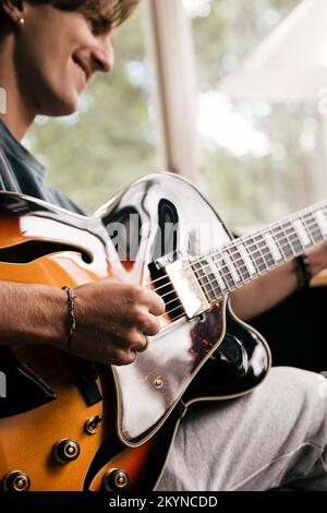 Die Hand eines lächelnden Mannes, der zu Hause Akkord auf der Gitarre spielt Stockfoto