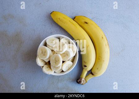 In einer Schüssel geschnittene Bananen, um einen Obstsalat mit ganzen Bananen an der Seite zuzubereiten. Obstbegriff und Gesundheit. Stockfoto