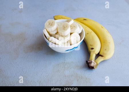 In einer Schüssel geschnittene Bananen, um einen Obstsalat mit ganzen Bananen an der Seite zuzubereiten. Obstbegriff und Gesundheit. Stockfoto