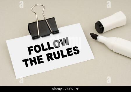 Finanz- und Geschäftskonzept. Auf einem grauen Hintergrund liegen eine Markierung und eine Visitenkarte mit der Aufschrift – BEFOLGEN SIE DIE REGELN Stockfoto