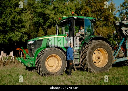 Ein Bauer sitzt im Traktor und spricht mit einem Mann, der an sonnigen Tagen an der Feile steht Stockfoto