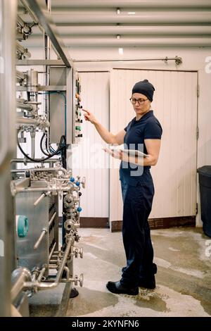 Landwirt, der einen digitalen Tablet-PC und eine Maschine in der Milchfabrik verwendet Stockfoto
