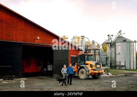 Reife Bauern mit Hund, der vor der Milchfabrik steht Stockfoto
