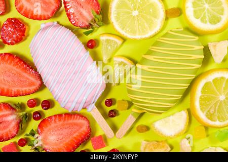 Zwei Eiscremes auf einem Stock - Erdbeere und Zitrone auf gelbem Hintergrund. Sommerliche Fruchtdesserts. Stockfoto