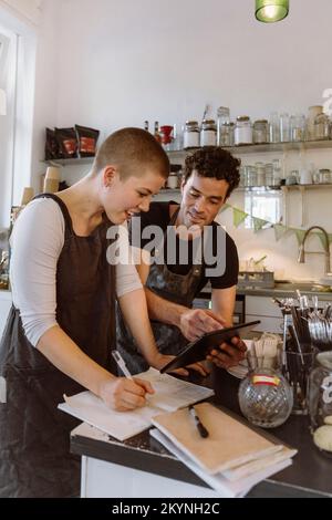 Männlicher Besitzer, der einen Tablet-PC mit einer Kollegin im Café teilt Stockfoto