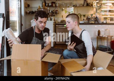 Junge Besitzerin mit Tablet-PC führt Inventur mit männlichem Kollegen im Café durch Stockfoto