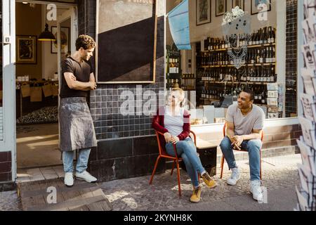 Kunden, die mit dem männlichen Besitzer sprechen, der am Eingang des Ladens steht Stockfoto
