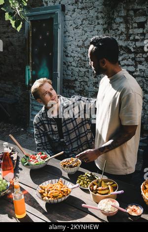 Junge männliche Freunde, die sich auf einer Gartenparty im Garten unterhalten Stockfoto