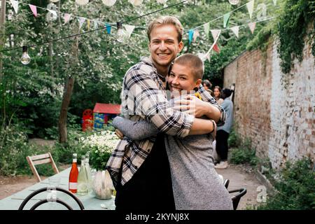 Seitenansicht von männlichen und weiblichen Freunden, die sich auf einer Dinnerparty im Garten umarmen Stockfoto