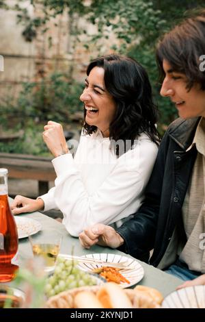 Glückliche Frau, die lachte, während sie mit einem männlichen Freund während der Dinnerparty am Esstisch saß Stockfoto