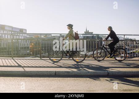 Seitenansicht für weibliche Geschäftsleute, die an sonnigen Tagen auf der Fahrspur fahren Stockfoto