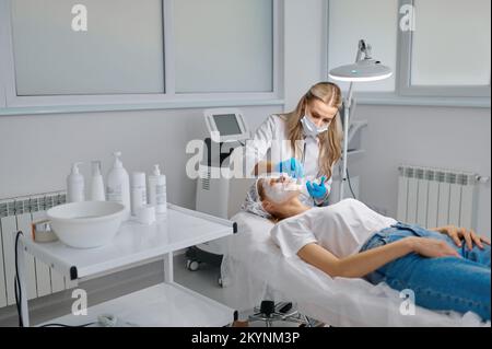 Kosmetikerin Anwendung Ton Gesichtsmaske auf Frau Gesicht Seitenansicht Stockfoto