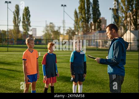 Junger Fußballtrainer, der Kindern auf dem Fußballfeld beibringt Stockfoto