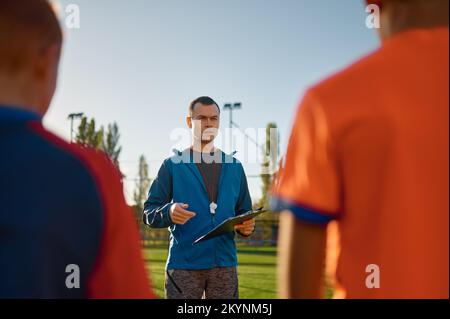 Junger Fußballtrainer, der Kindern auf dem Fußballfeld beibringt Stockfoto