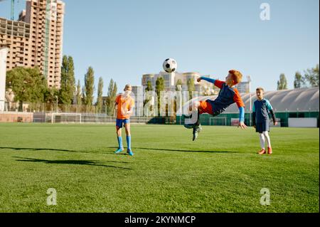 Junior Forward springt mit Bein zum Kickball und nimmt am Fußballspiel Teil Stockfoto