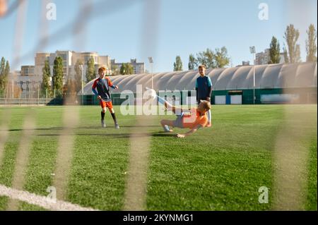 Junior Forward springt mit Bein zum Kickball und nimmt am Fußballspiel Teil Stockfoto