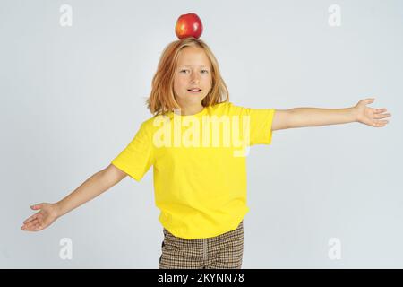 Ein Teenager in einem gelben T-Shirt hält einen Apfel auf dem Kopf. Isolierter Hintergrund. Bildungskonzept. Stockfoto