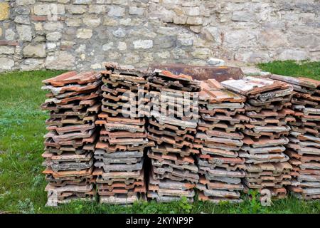 Alte Tonfliesen sind auf grünem Gras gestapelt, vor dem Hintergrund einer alten Steinwand. Speicherplatz kopieren. Selektiver Fokus. Stockfoto
