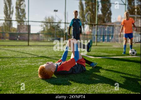 Kleiner Fußballspieler mit verletzten Knien, der auf dem Feld liegt Stockfoto