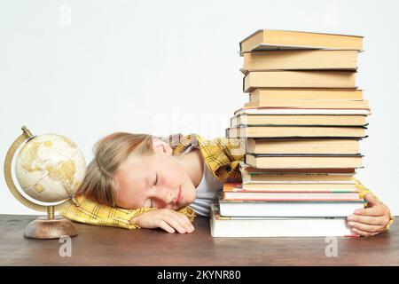 Bildungskonzept. Das Teenager-Mädchen schlief bei den Hausaufgaben ein. Neben dem Schüler auf dem Tisch liegen Bücher und ein Globus. Stockfoto