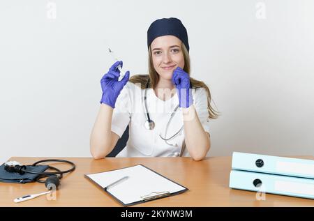 Medizin und Gesundheitskonzept. Eine junge Ärztin sitzt am Tisch und bereitet eine Spritze mit Medikamenten für die Injektion vor. Isoliert auf weißem Hintergrund. Stockfoto