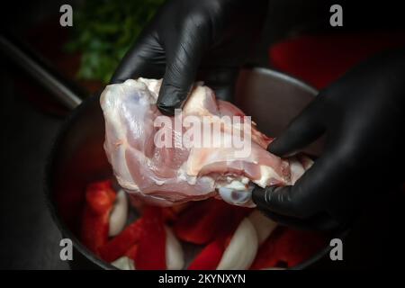 Die Hände des Küchenchefs in schwarzen Handschuhen halten rohes Fleisch auf dunklem Hintergrund. Geringe Schärfentiefe Stockfoto
