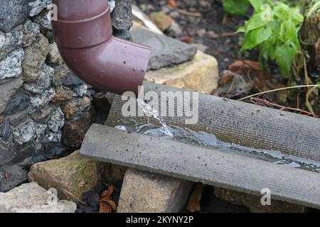 Regenwasser fließt aus der Dachrinne. Dachrinnen-System auf dem Landhaus. Stockfoto