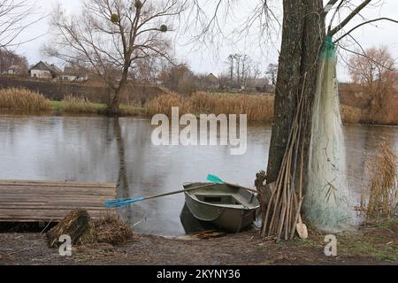Blick auf einen gefrorenen See mit glattem Eis. Ruderboot und Fischernetze in der Nähe des Sees. Stockfoto