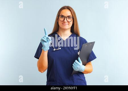 Frau Doktor mit Stethoskop und Klemmbrett, die mit dem Finger nach oben zeigt Stockfoto