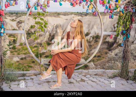 Junge Frau, die das Tal mit Felsformationen und Feenhöhlen in der Nähe von Goreme in Kappadokien, Türkei, erkundet. Wunschbaum. Kleine mehrfarbige Kannen mit Stockfoto