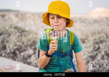 Tourismusjunge, der türkisches Eis isst, während er das Tal mit Felsformationen und Feenhöhlen in der Nähe von Goreme in Kappadokien, Türkei, erkundet Stockfoto