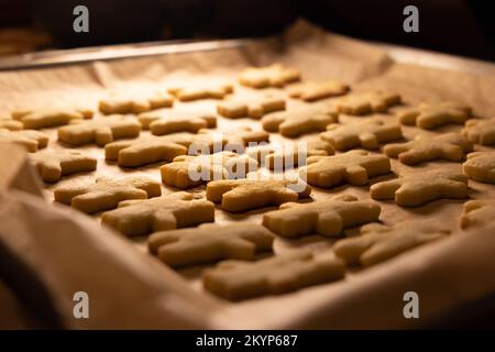 Nahaufnahme einer Pfanne mit frisch gebackenen hausgemachten weihnachtskeksen, Hintergrundbeleuchtung, verschwommenem Hintergrund, Kekse in Form von kleinen Figuren Stockfoto