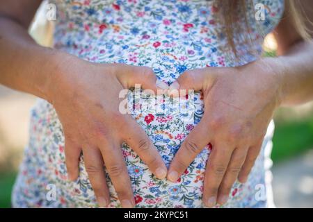 Schwangere Frau, die mit ihren Fingern ein Herz bildet Stockfoto