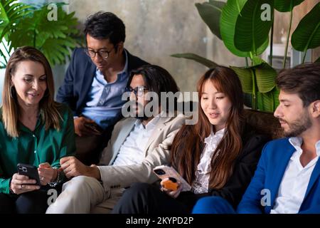 Firmenporträt von Geschäftsleuten, die sich auf der Couch entspannen - multiethnisches Business-Team, das Videos auf dem Smartphone ansieht Stockfoto