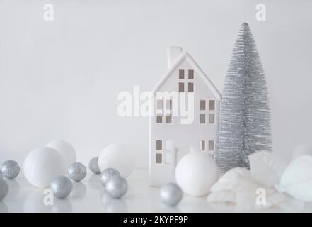 Weihnachtskomposition. Weihnachtskugeln weiß und silber, dekoratives Haus, weihnachtsbaum auf weißem Hintergrund Stockfoto