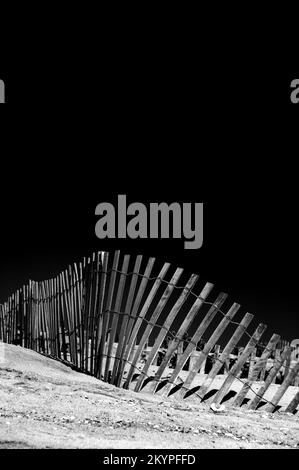 Gedrehter Zaun an einem Sandstrand. Schwarzweißfotografie Stockfoto