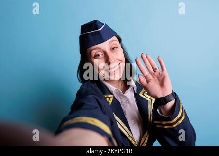 Lächelnde Stewardess, die Selfie aus der ersten Person macht, Flugbegleiter macht Foto mit Smartphone-Frontkamera, fpv. Junge attraktive Flugbegleiterin im Uniform-Porträt der Flugzeugarbeiter Stockfoto