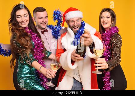 Gruppe oder Gesellschaft von Freunden zusammen mit dem Weihnachtsmann feiern Weihnachten, haben Spaß und offenen Champagner mit Gläsern. Stockfoto