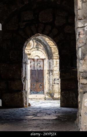 Geheimnisvoller alter Steinbogen führt zum Eingang des Motsameta-Klosters in Imereti, Georgia, mit alten hölzernen Türen mit Heiligen David Stockfoto