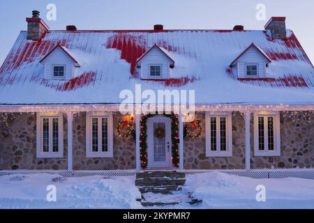 Beleuchtetes zweistöckiges Haus aus Feldstein im Canadiana-Stil dekoriert mit Weihnachtskränzen und Lichtern in der Dämmerung. Stockfoto
