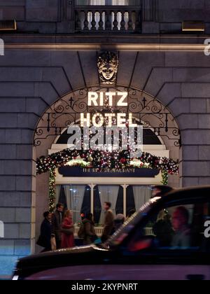 Weihnachtsausstellung Im Ritz Hotel. Fußgänger kommen vorbei, und ein Taxi fährt unscharf durch die Bewegung, wobei Lichter in der Windschutzscheibe reflektieren. Stockfoto